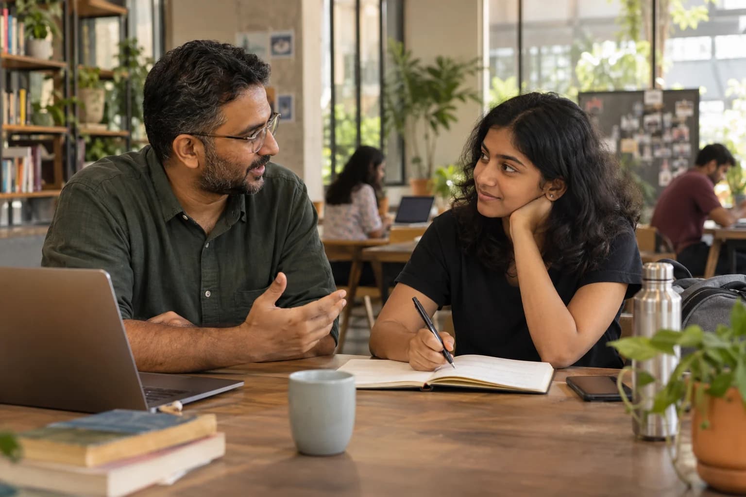 A mentor and young adult discuss goals together over an open notebook in a community workspace.
