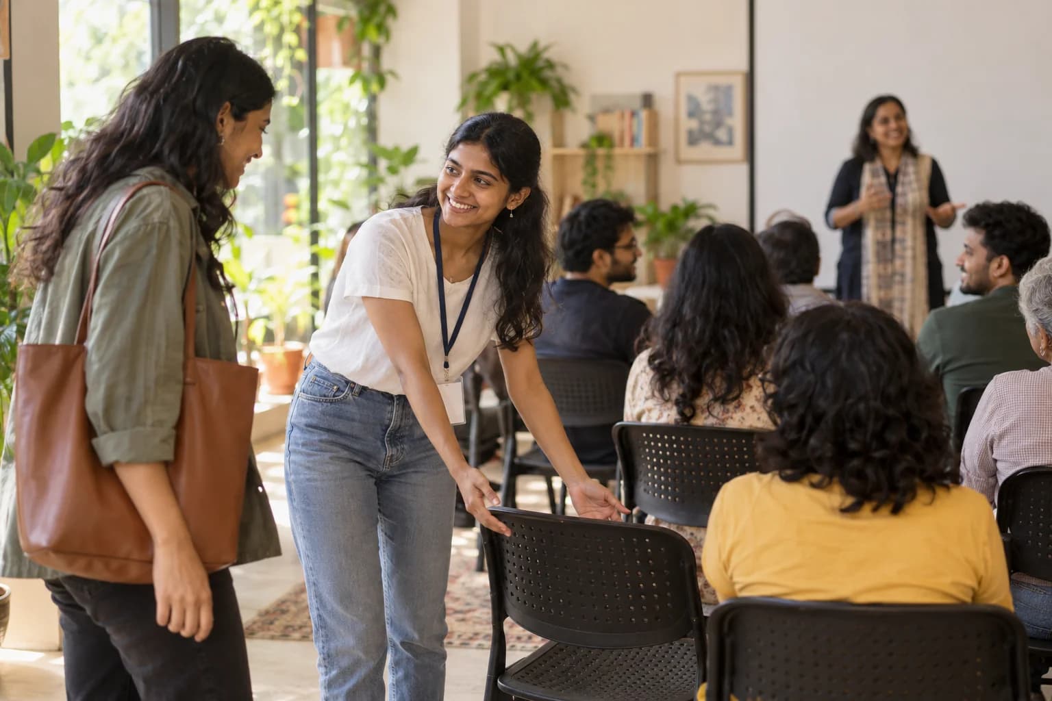 A volunteer welcomes a new participant and offers a chair at a community session